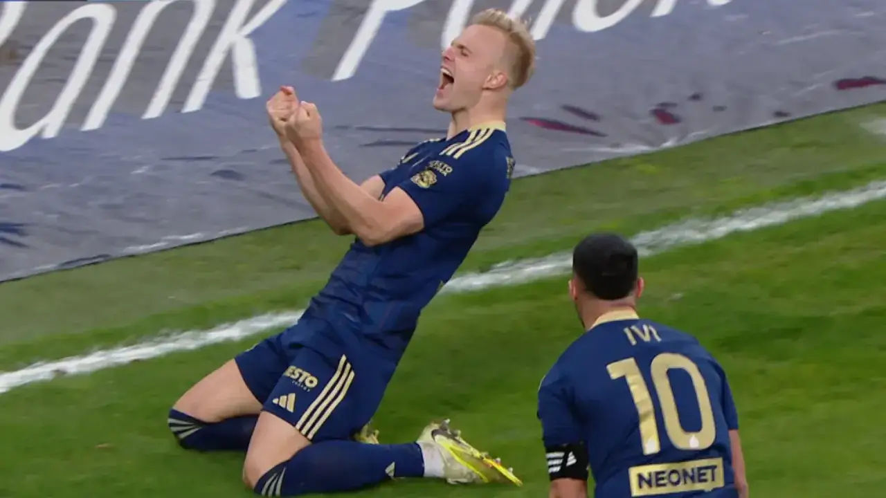 Piłkarz w niebieskiej koszulce z żółtymi pasami radośnie klęczy na boisku. Chcesz wiedzieć, gdzie oglądać Ekstraklasę?