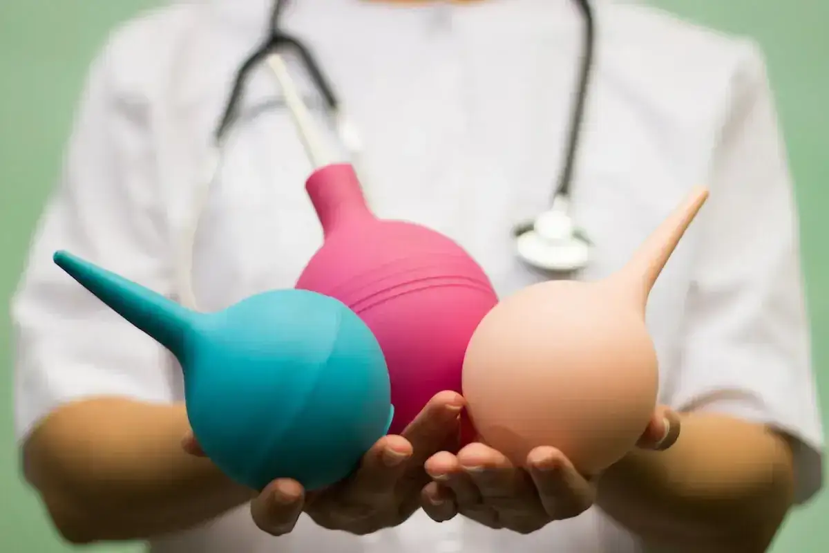 Trzy gruszki medyczne w dłoniach, przygotowane do lewatywy przed porodem.
