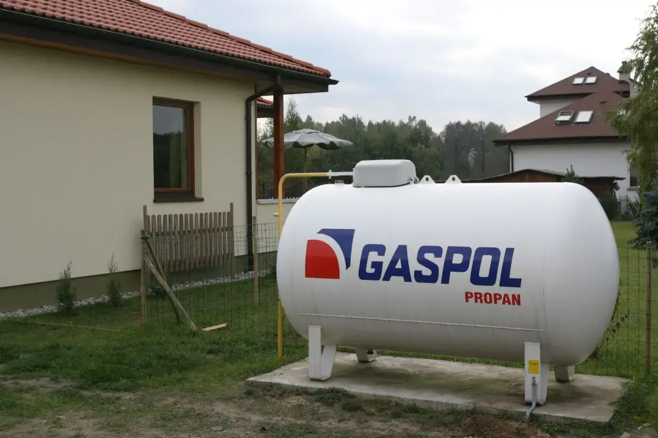 Duży, biały zbiornik z napisem GASPOL PROPAN, kt&oacute;ry jest źr&oacute;dłem ogrzewania dla domu.