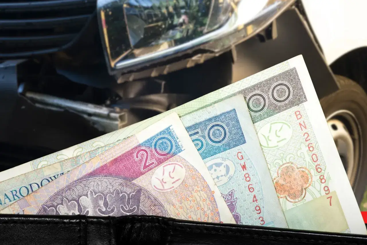 Portfel z polskimi banknotami na tle uszkodzonego samochodu. Czy to symbol ulgi dla niepełnosprawnych przy rejestracji samochodu?