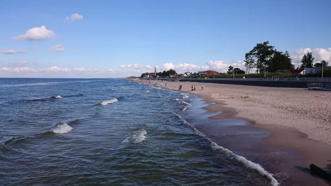 Spokojne morze i piaszczysta plaża w Sarbinowie. Ludzie spacerują brzegiem, ciesząc się letnim dniem nad Bałtykiem.