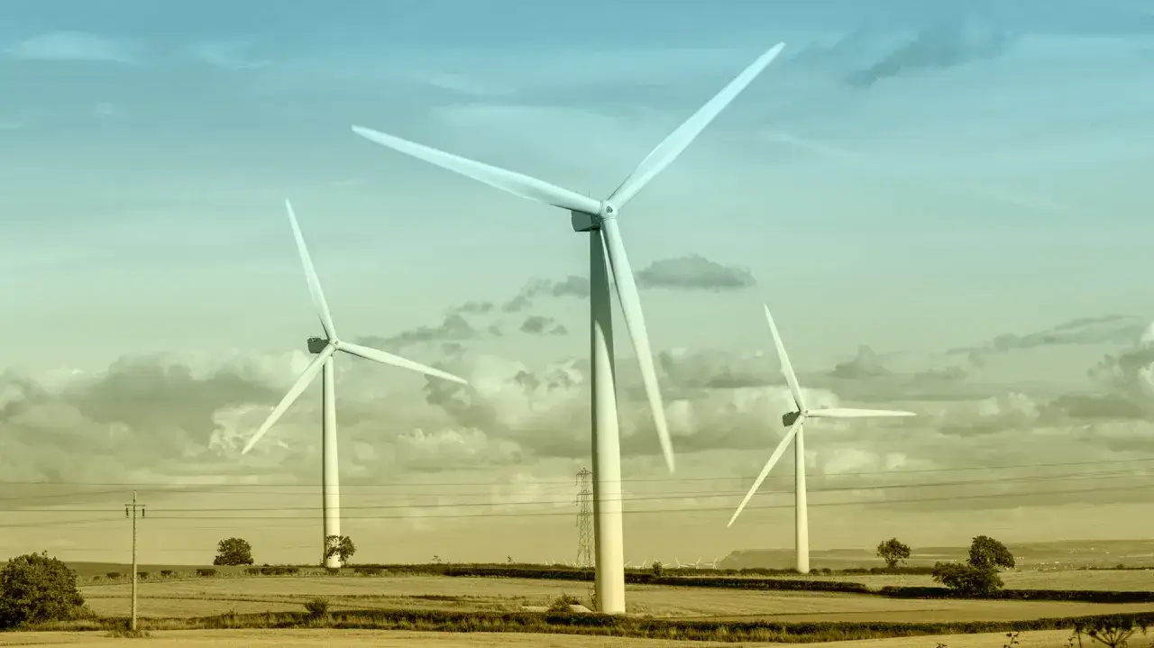 Trzy wiatraki na tle nieba z chmurami. Wiatraki symbolizują czystą energię i zalety elektrowni wiatrowej dla środowiska.