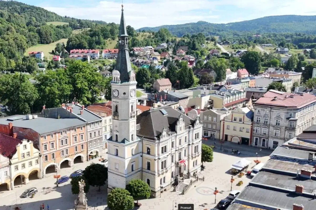 Rynek w Lądku-Zdroju z ratuszem i wieżą zegarową, otoczony zabytkową zabudową. W tle zielone wzg&oacute;rza. To gł&oacute;wne lądek zdr&oacute;j atrakcje.