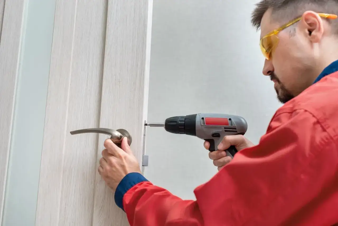 Mężczyzna w okularach ochronnych pokazuje, jak wymienić klamkę w drzwiach wewnętrznych, używając wkrętarki.