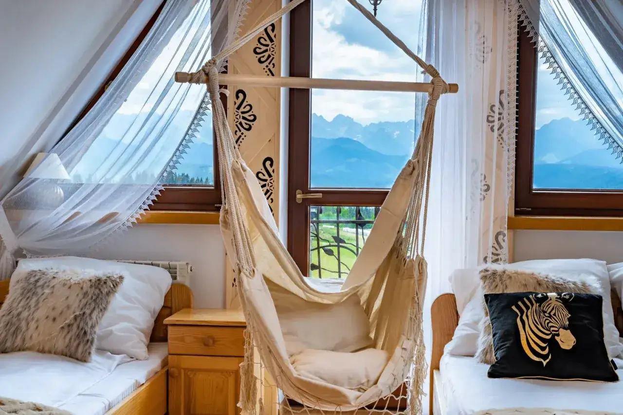 Willa G&oacute;rski Wierch: przytulny pok&oacute;j z hamakiem i widokiem na g&oacute;ry. Dwa ł&oacute;żka, drewniane meble i ozdobne zasłony tworzą g&oacute;rski klimat.