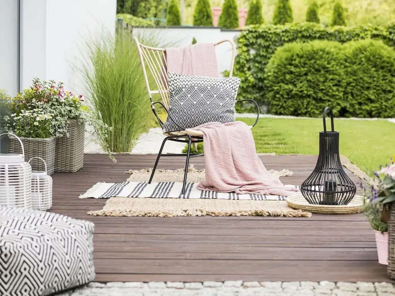 Przytulny ogródek na parterze w bloku. Krzesło z poduszką i kocem, obok latarnia i donice z kwiatami.