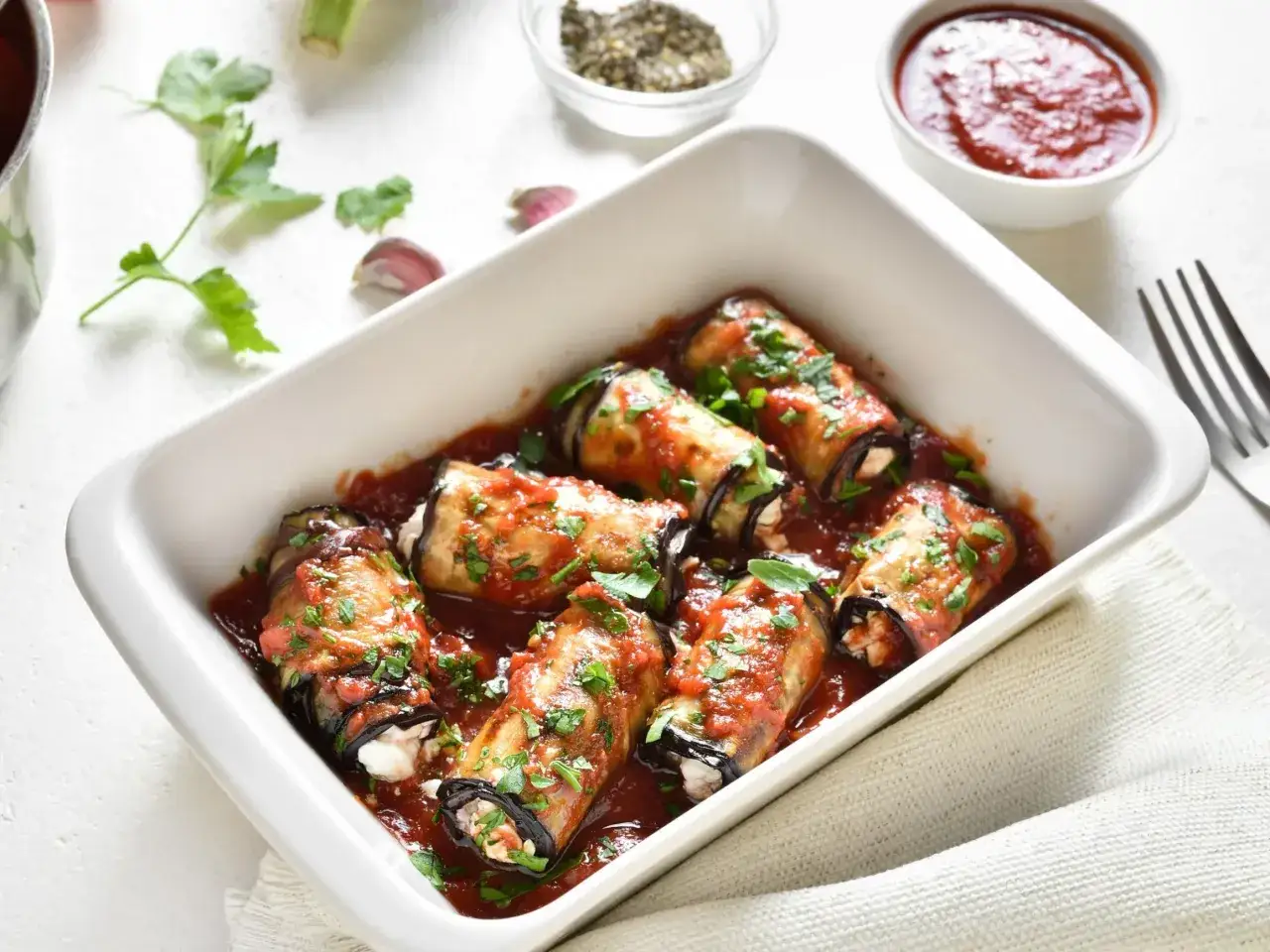 Pyszne roladki z bakłażana w sosie pomidorowym, posypane natką pietruszki, gotowe do podania.