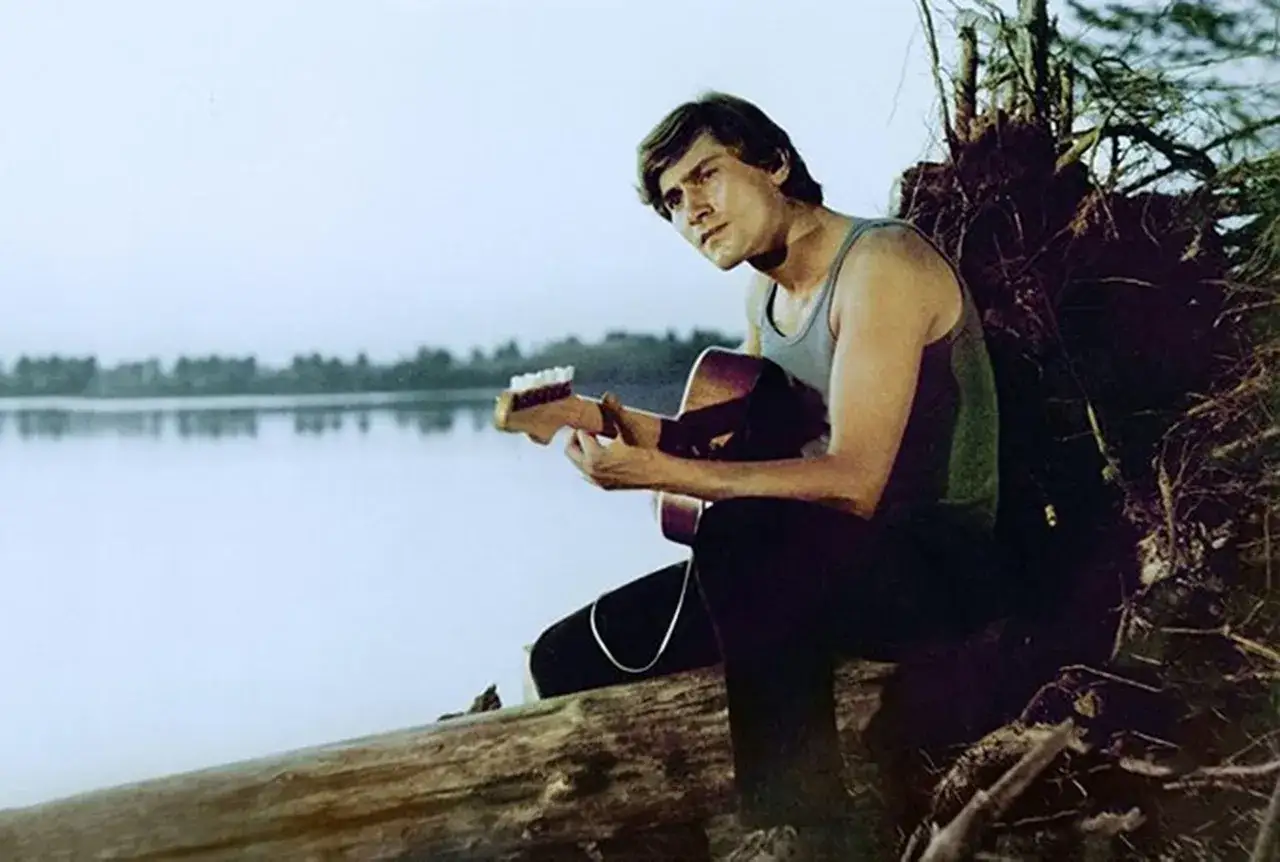 Młody mężczyzna z gitarą siedzi na powalonym drzewie nad jeziorem. To scena z filmu, gdzie kręcono Karate po polsku.