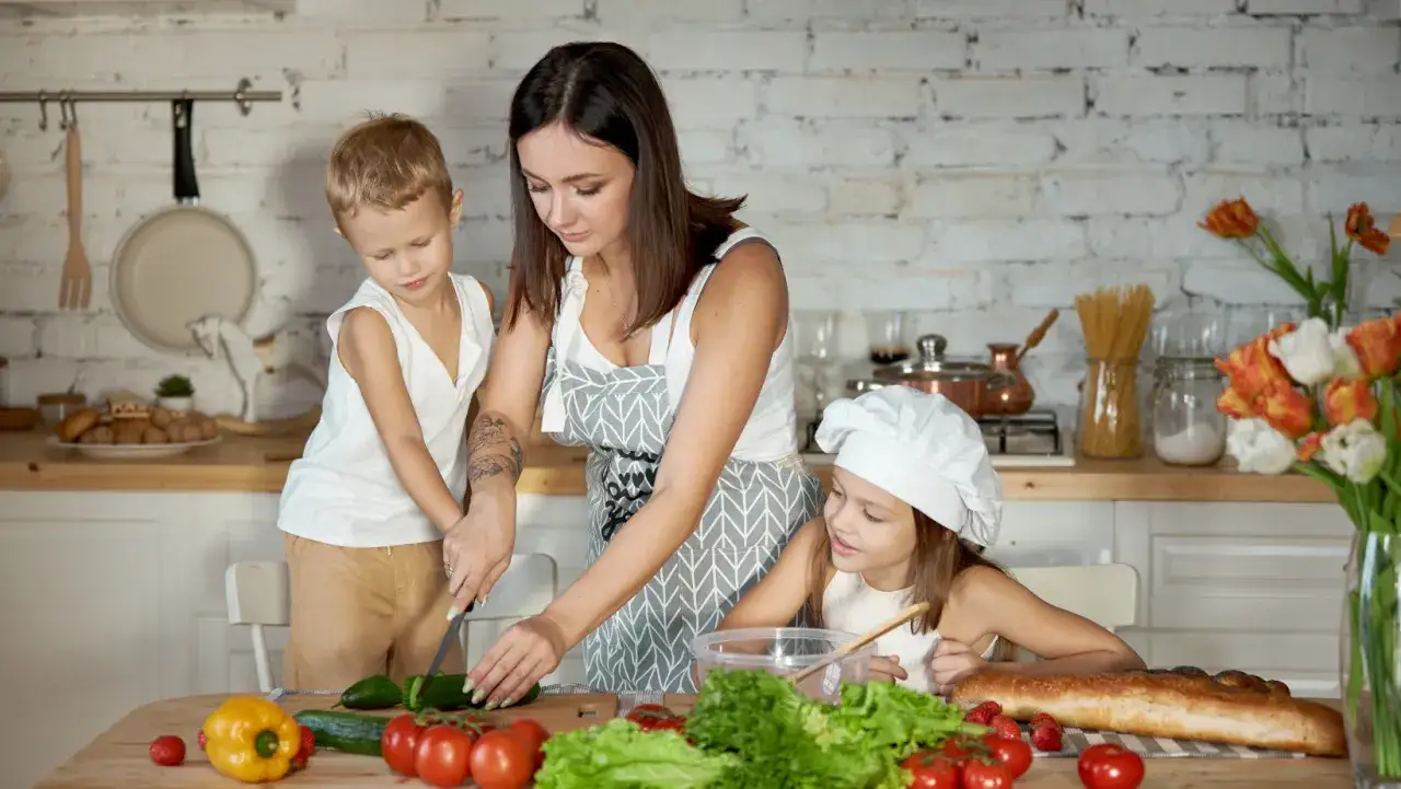 Rodzina przygotowuje posiłek w kuchni, co oznacza self catering. Dzieci pomagają mamie kroić warzywa.