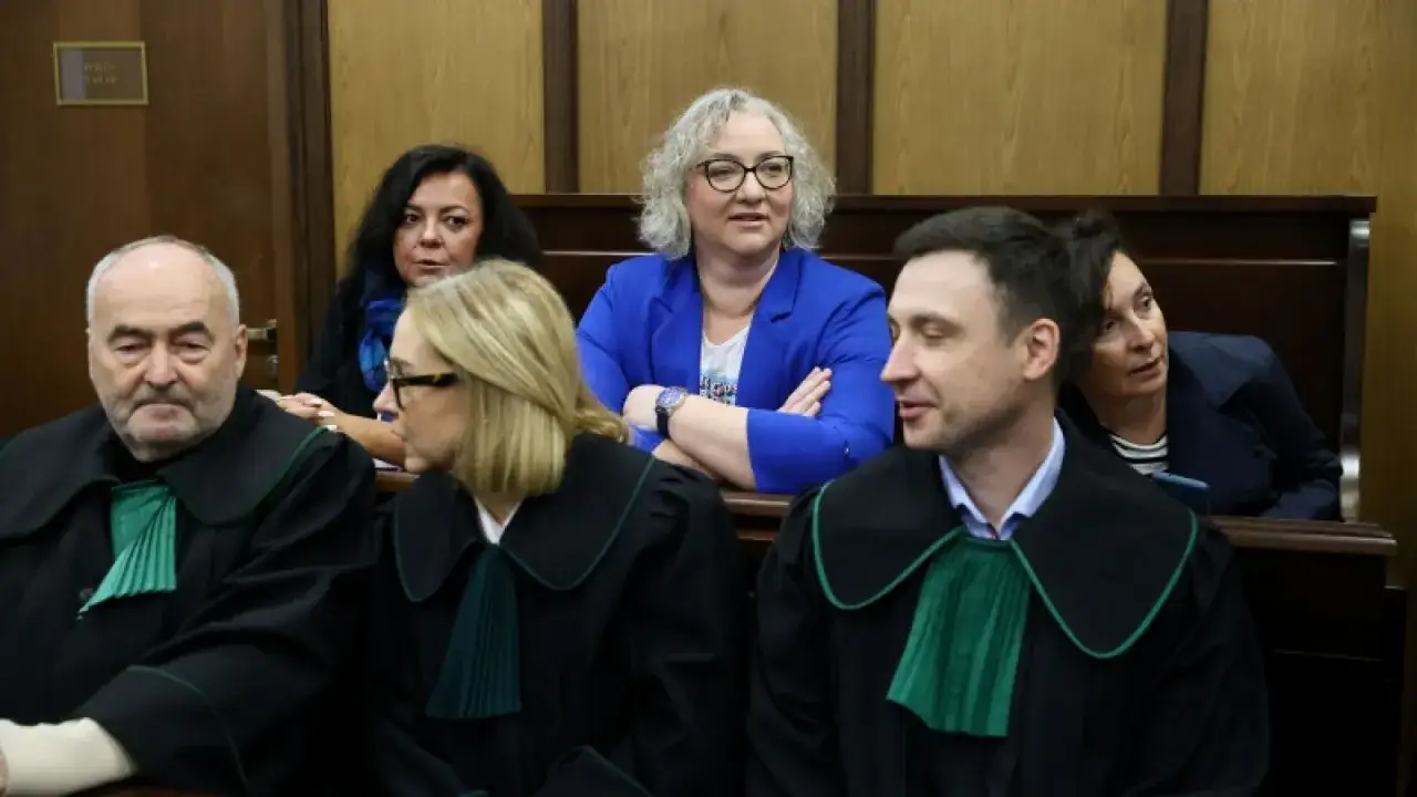 Sędzia w niebieskiej marynarce i prawnicy w togach, czekają na rozprawę.