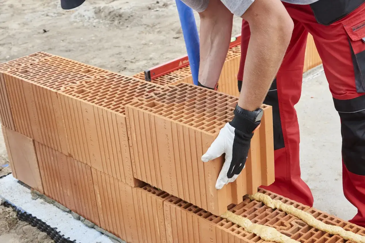 Budowlaniec układa pustaki ceramiczne, stosując murowanie na piankę. Nowoczesna technika budowy.