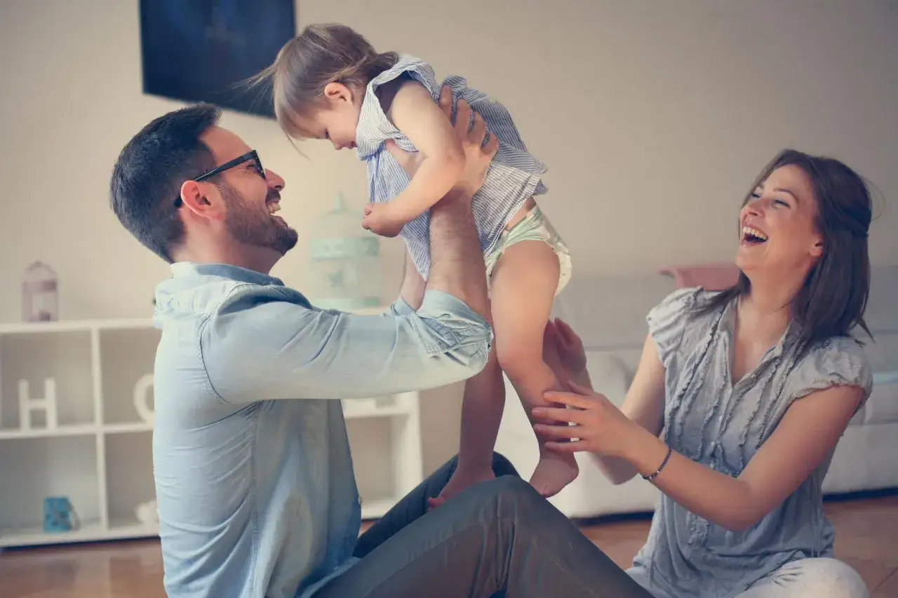 Szczęśliwi rodzice bawią się z dzieckiem. Marzysz o tym, jak adoptować dziecko? To zdjęcie pokazuje miłość i radość, która może być Twoja.