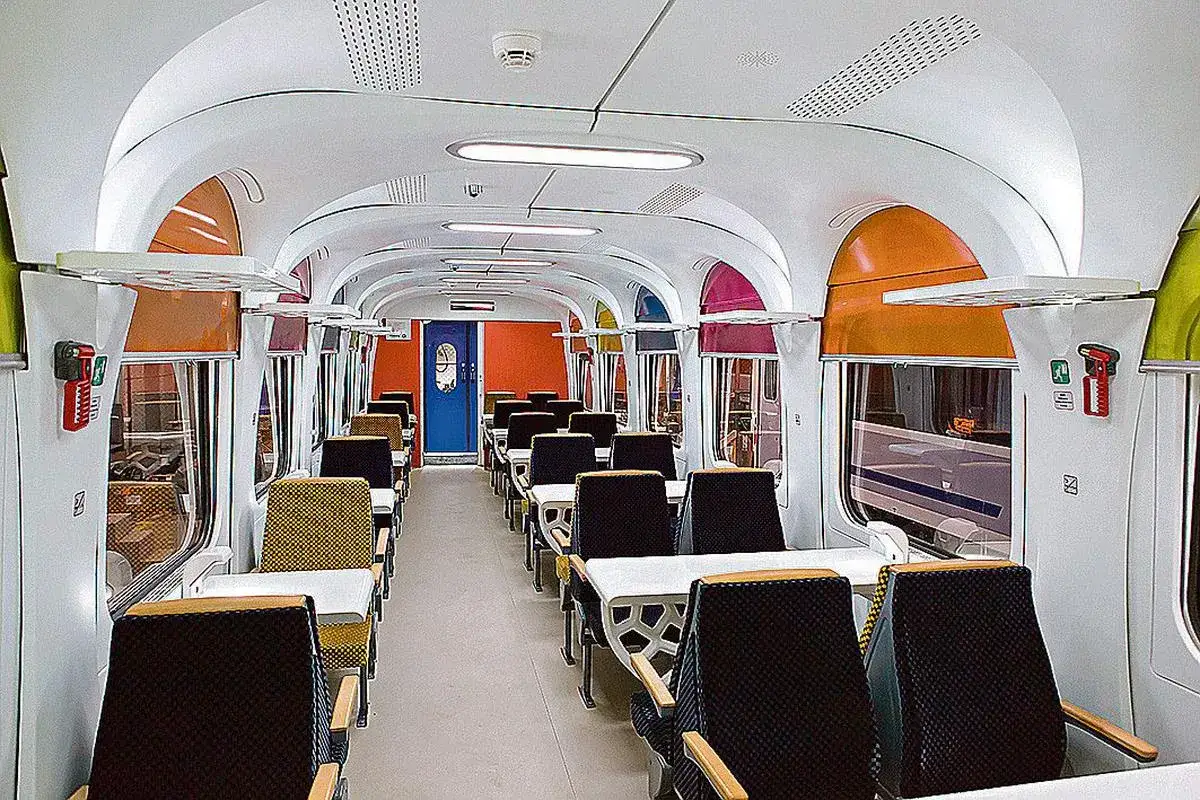 Wnętrze nowoczesnego wagonu kolejowego z kolorowymi akcentami. Czy TLK to Intercity? Wygodne siedzenia i stoliki zapraszają do podróży.