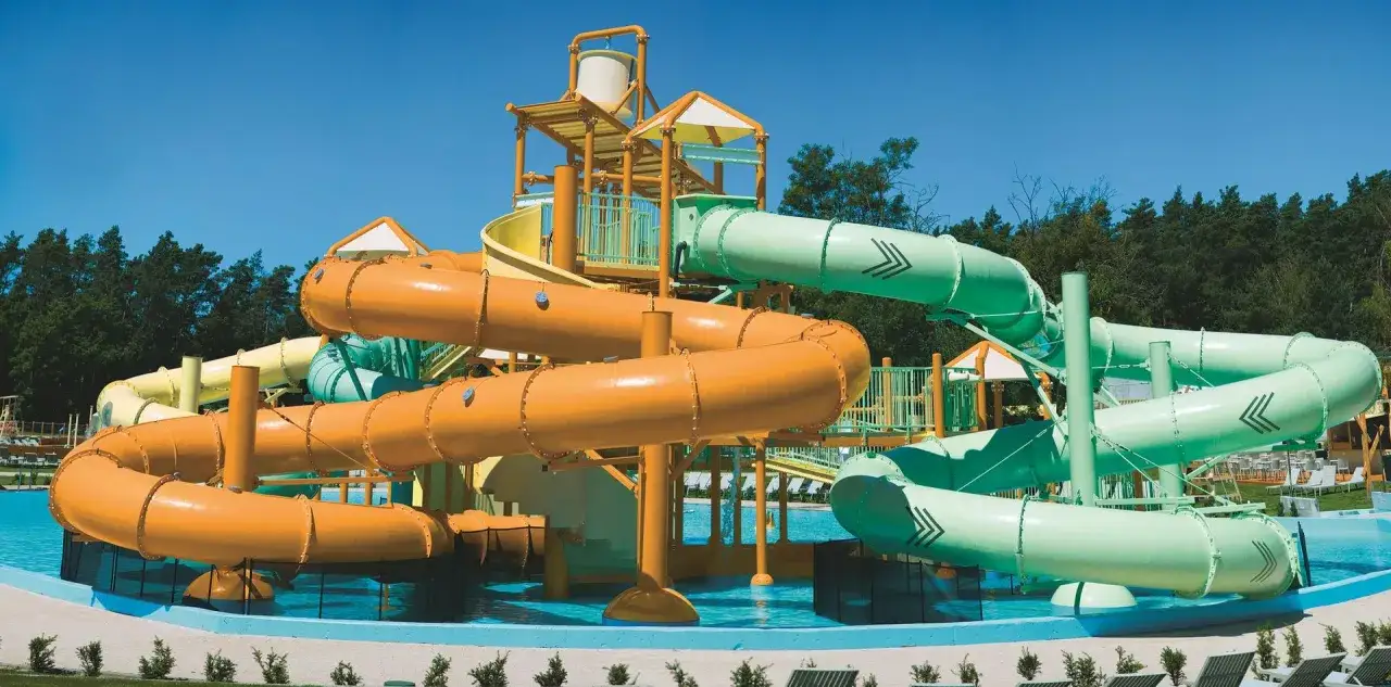 Kolorowy park wodny z pomarańczowymi i zielonymi zjeżdżalniami, idealny na wakacje z bonem turystycznym.