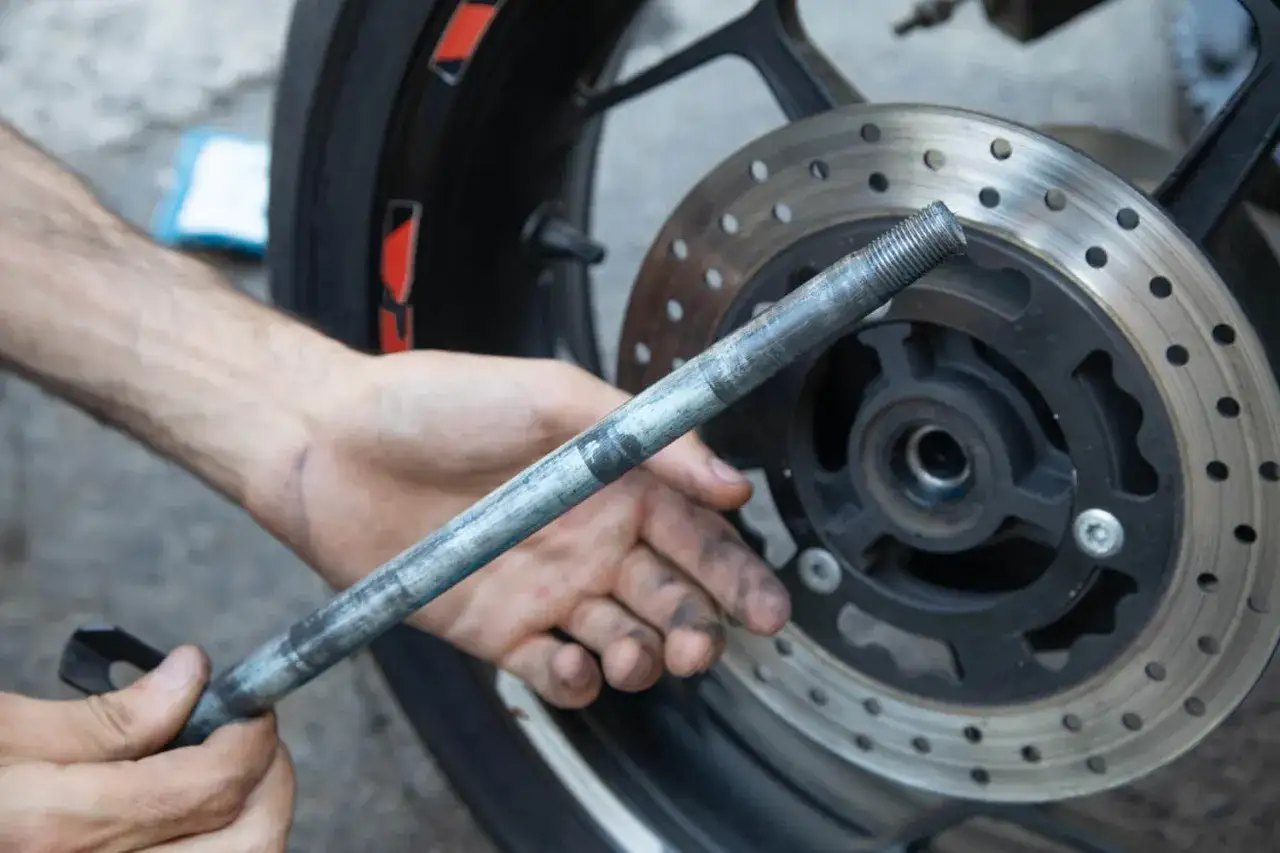 Ręce mechanika przy kole motocykla, przygotowującego się do naprawy, gdzie klocek hamulcowy nie odbija od tarczy.