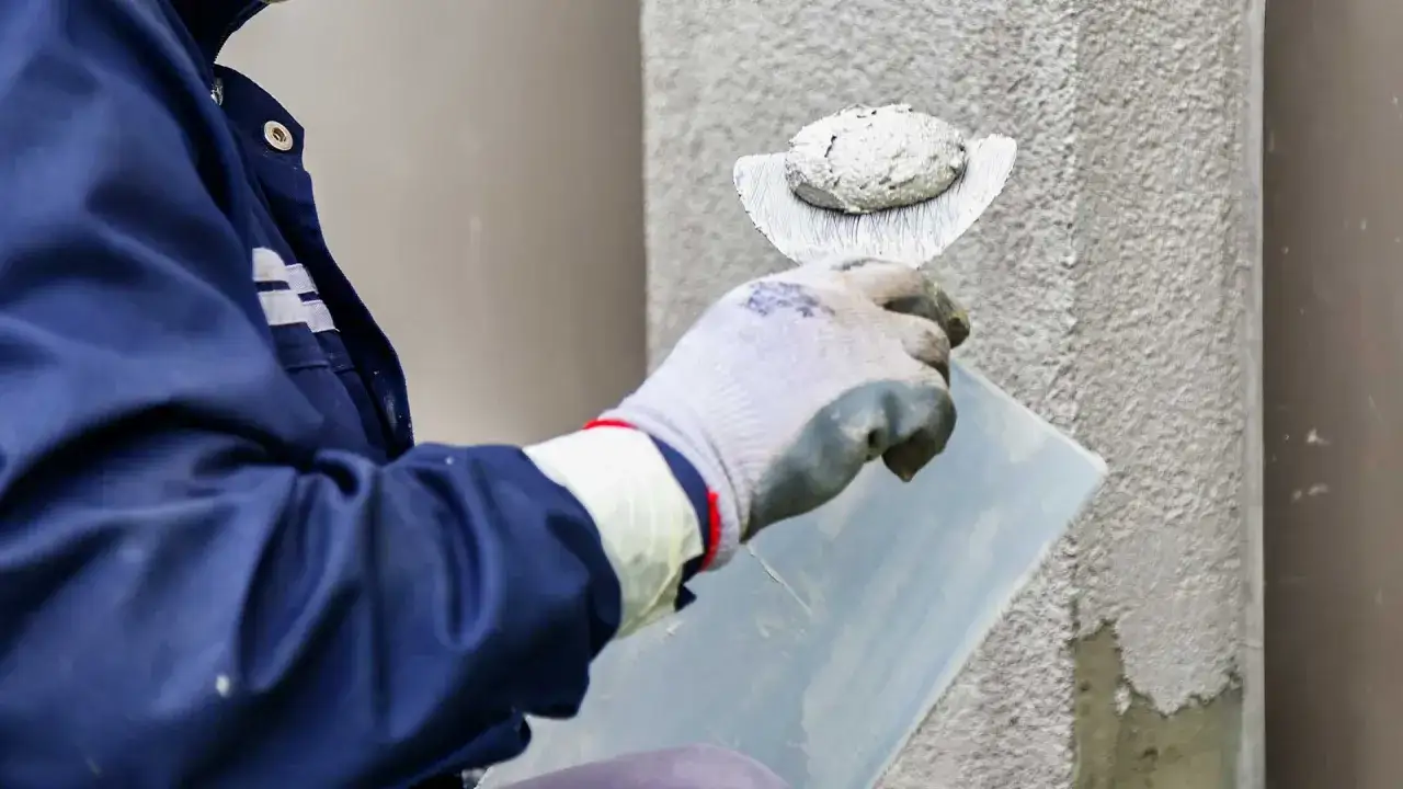 Tynkarz w rękawicach nakłada zaprawę na ścianę. Zastanawiasz się, ile kosztuje metr tynkowania?