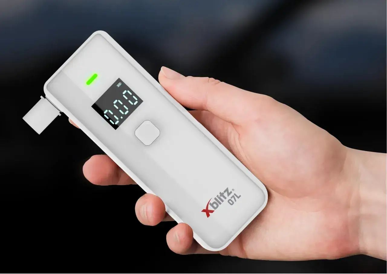 Dłoń trzyma alkomat Xblitz 07L z wynikiem 0.00. Pytanie 