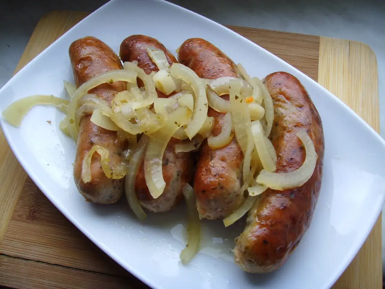 Złociste białe kiełbaski w piwie, podane z duszonymi cebulkami na białym talerzu. Pyszne danie!