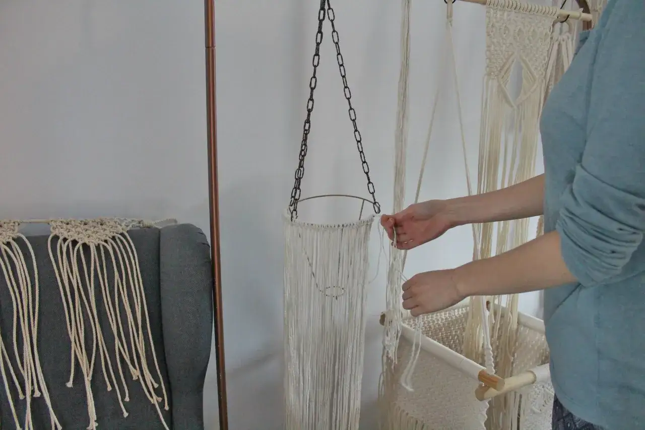 Ręce tworzą lampę ze sznurka, dodając kolejne pętelki do makramowego klosza.