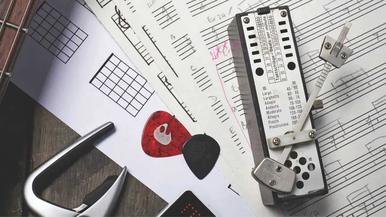 Metronom i nuty pomagają zrozumieć, jak liczyć takty w muzyce. Gitara, kostki i kapodaster dopełniają scenę.