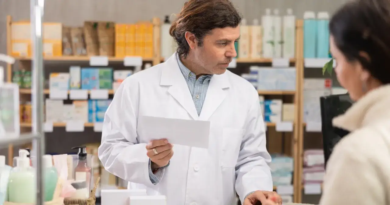 Farmaceuta w białym kitlu trzyma receptę, pomagając klientce dowiedzieć się, jak sprawdzić, co jest na recepcie.