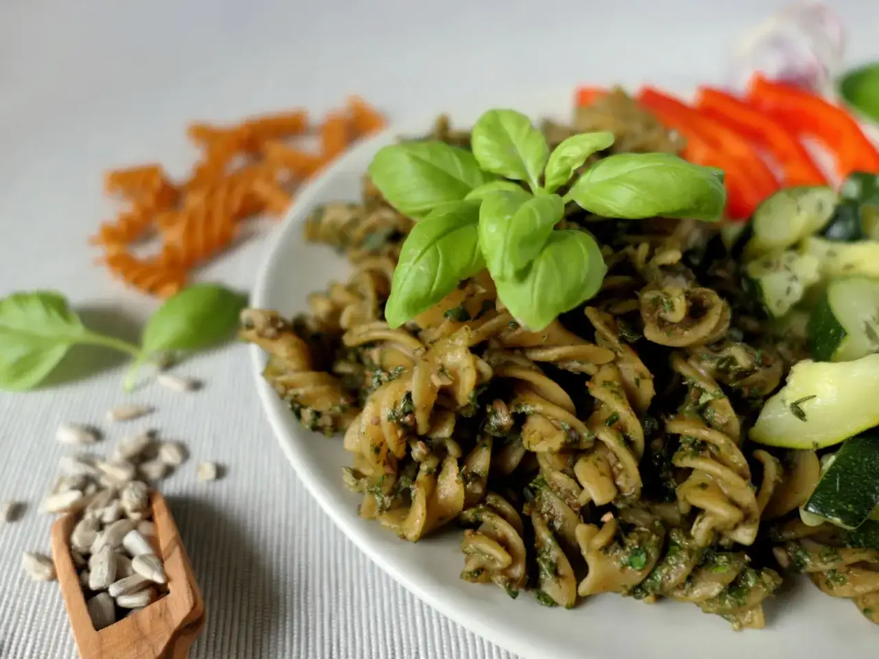 Makaron z aromatycznym pesto bazyliowym, podany z cukinią i papryką. Na talerzu świeże listki bazylii.