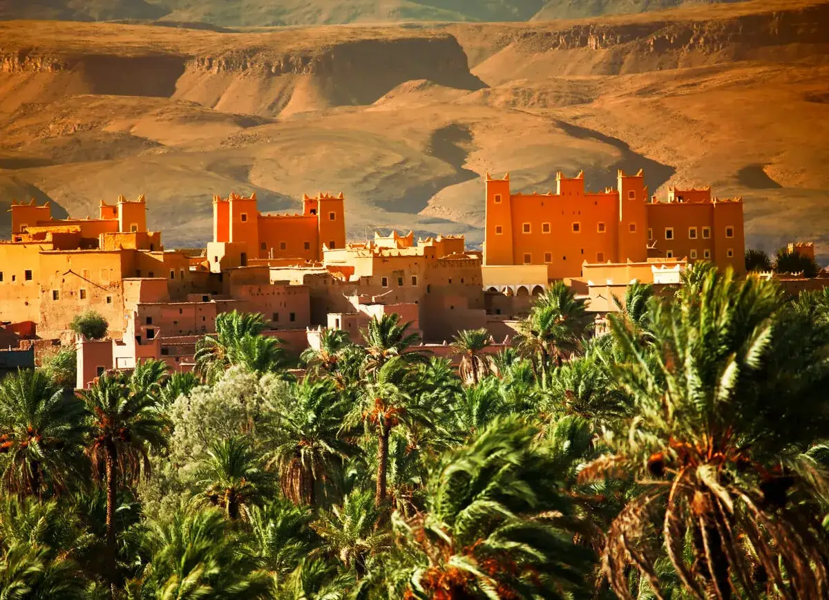 Maroko co warto wiedzieć: Kasba Ait Ben Haddou, twierdza z gliny, otoczona palmami, w sercu pustynnego krajobrazu.