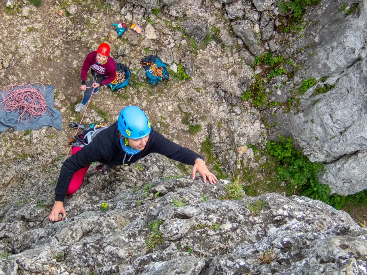 Dwie osoby w kaskach wspinają się po skale. Jedna z nich, na pierwszym planie, w niebieskim kasku, wspina się wyżej. To część ich kursu taternickiego.