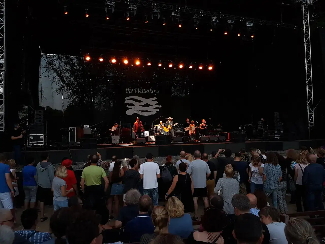 Zespół ośmiu muzyków The Waterboys gra na scenie podczas koncertu.