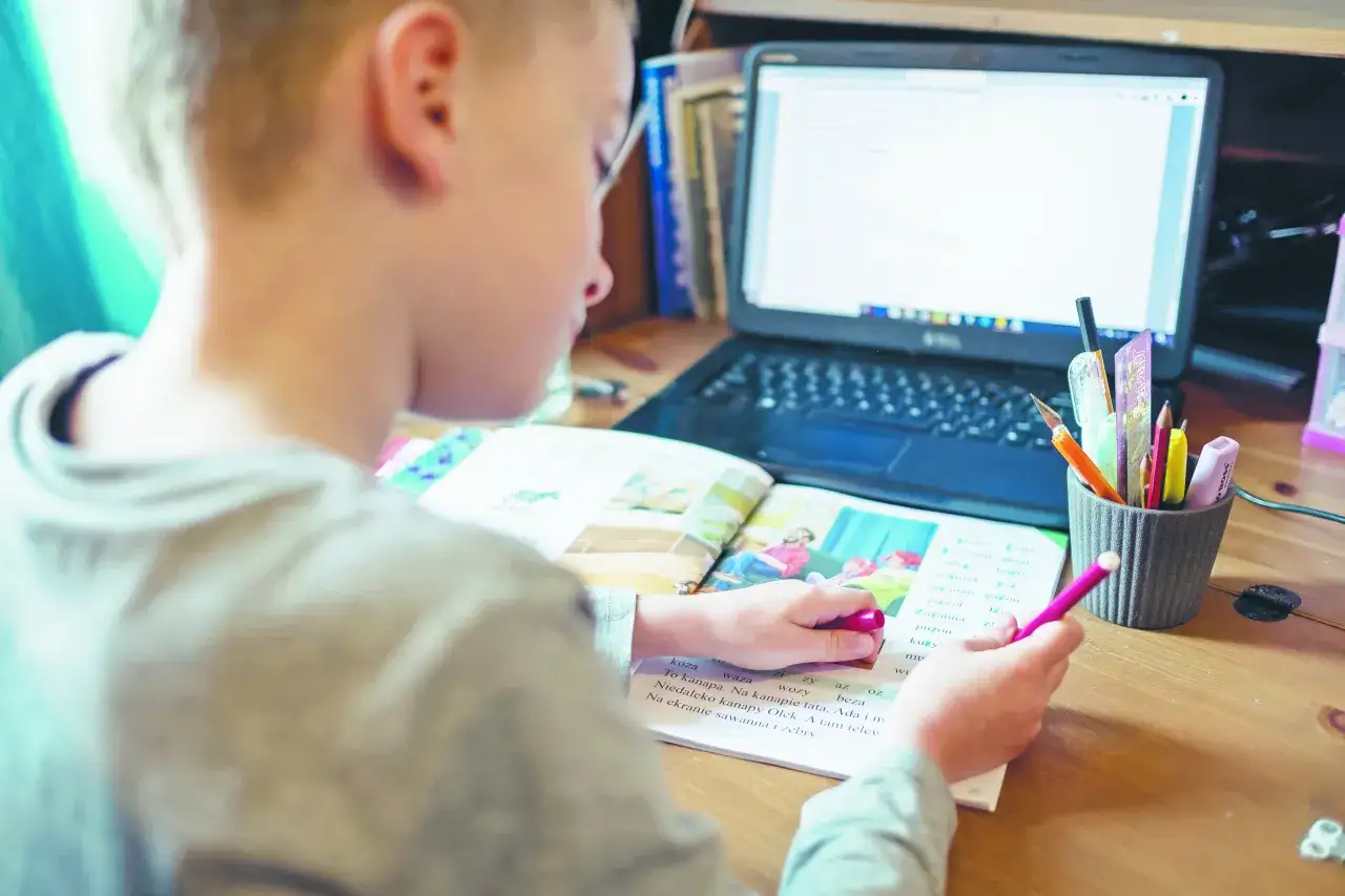 Chłopiec uczy się zdalnie, pisząc w zeszycie przy laptopie. Zastanawia się, ile trwało zdalne nauczanie.