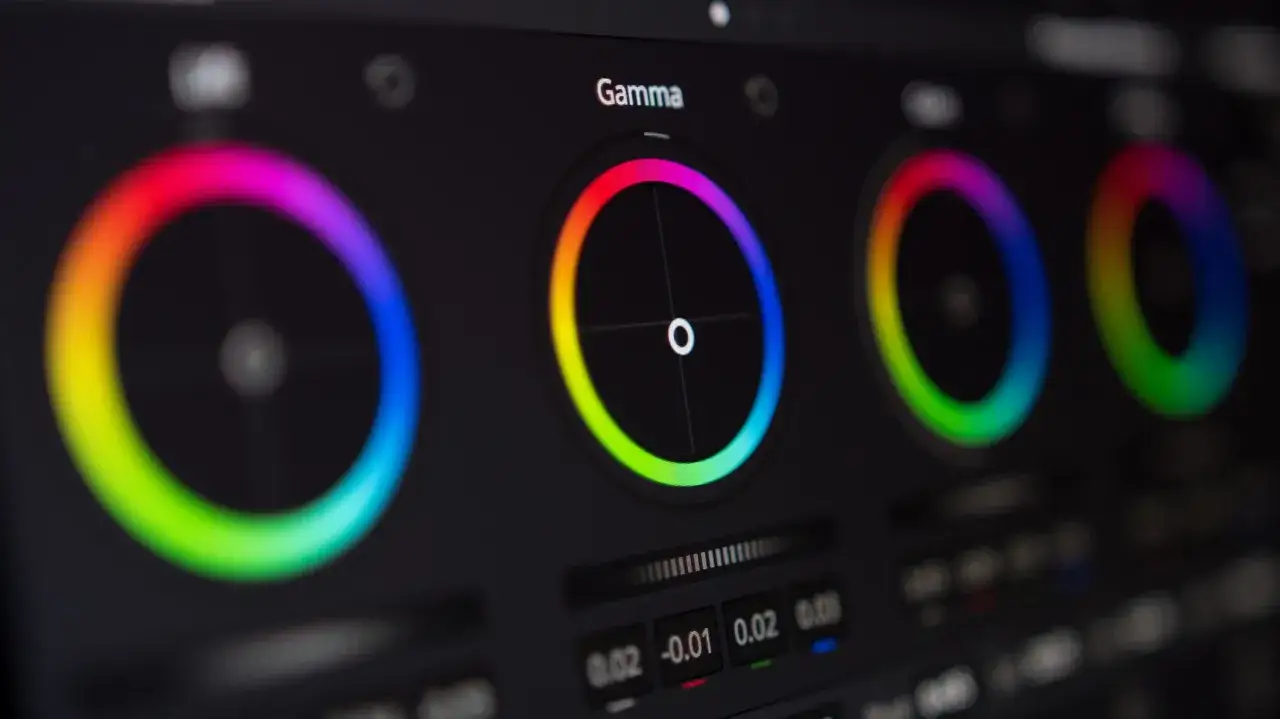 Producenci na planie filmowym dopracowują kolory na monitorze. Widoczne koła barw i suwaki pokazują proces korekcji barwnej.