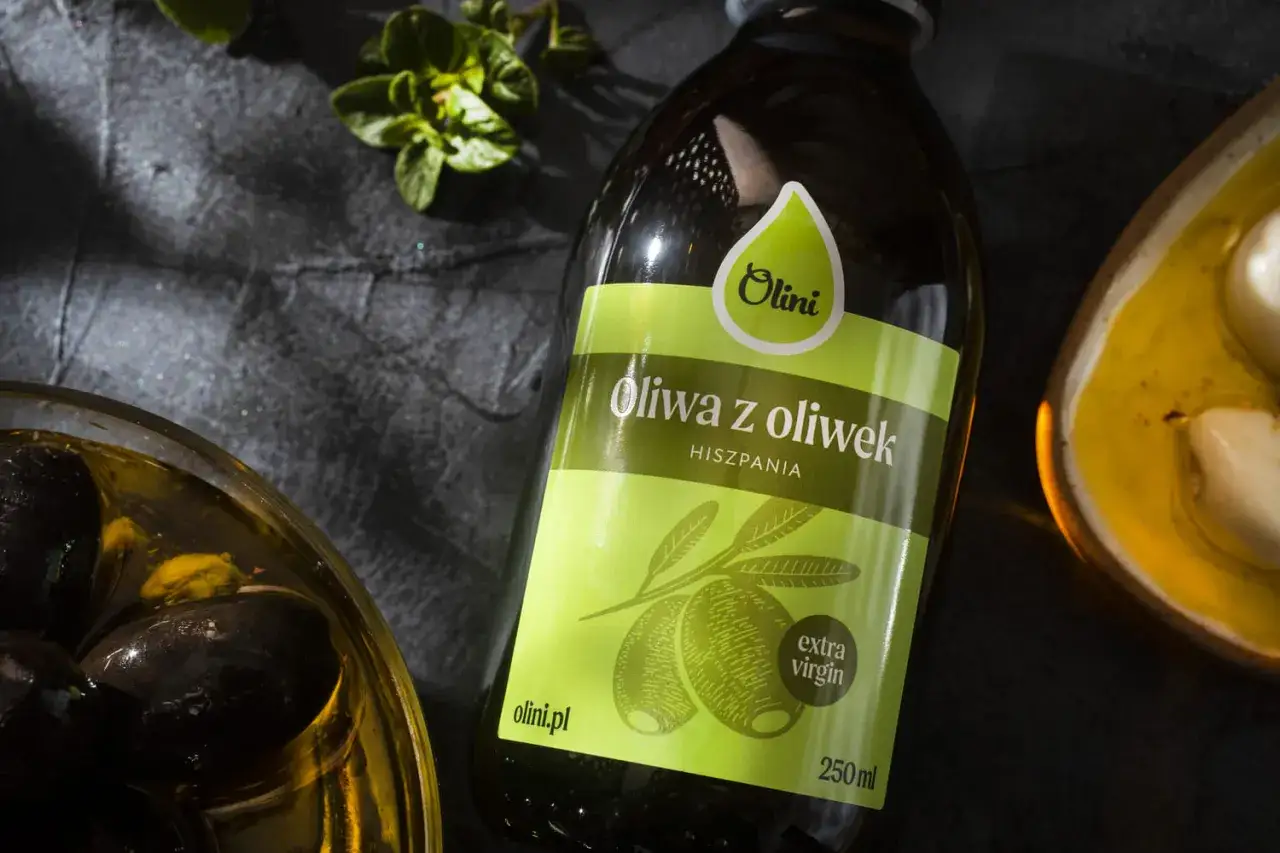 Oliwa z oliwek na twarz? Ta hiszpańska extra virgin Olini to sekret pięknej sk&oacute;ry. Obok czarne oliwki i czosnek.