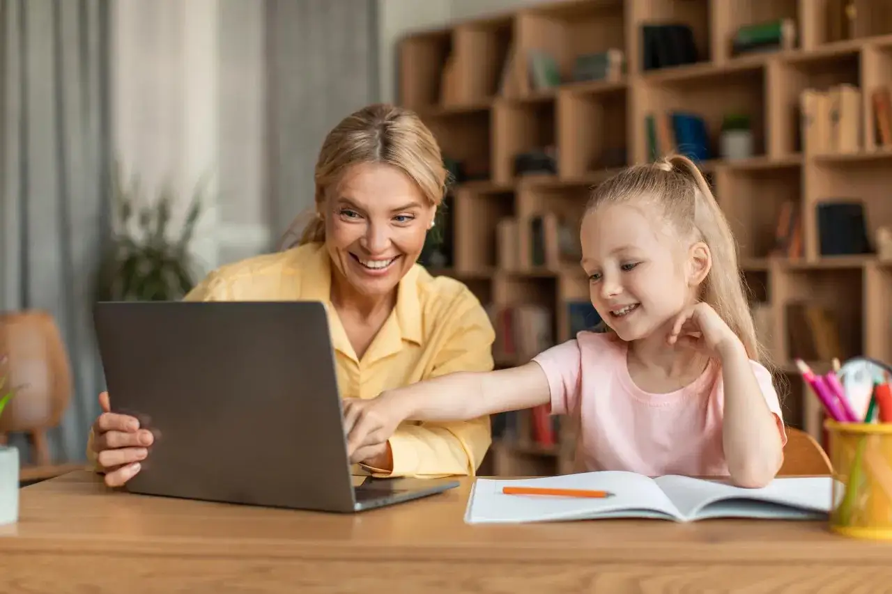 Uśmiechnięta mama i córka uczą się razem, odkrywając zalety i wady edukacji domowej.