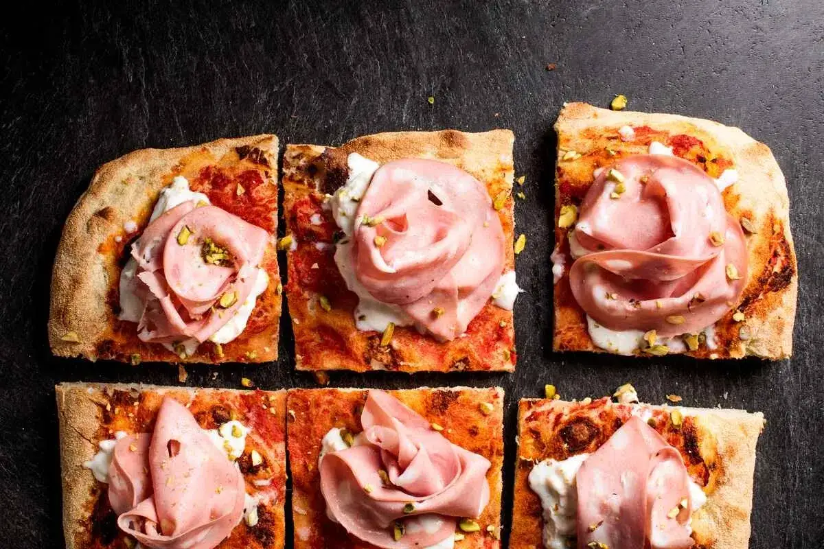 Kawałki pizzy rzymskiej z mortadelą, kremowym serem i pistacjami. Idealny przepis na pizza rzymska!