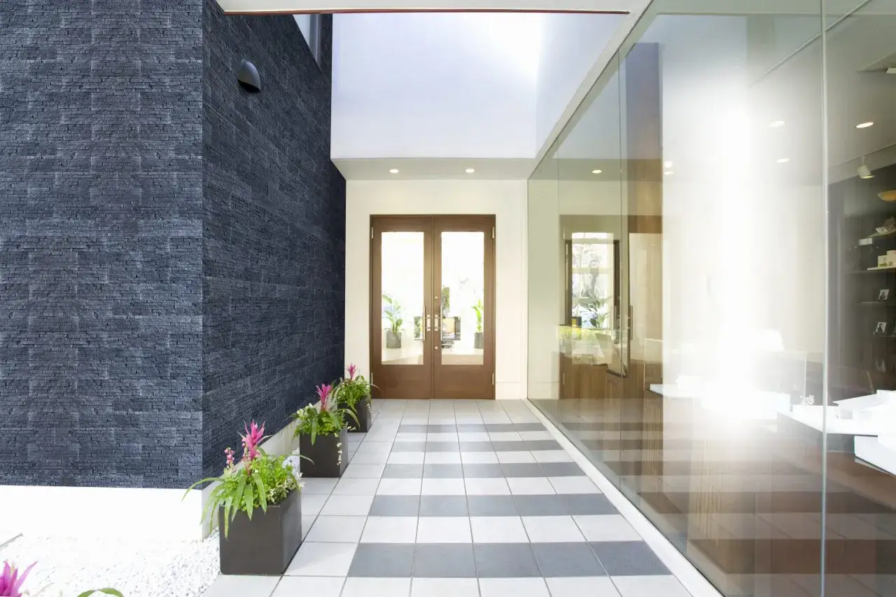 Nowoczesna klatka schodowa w domu z kamienną ścianą, szklaną elewacją i donicami z kwiatami.