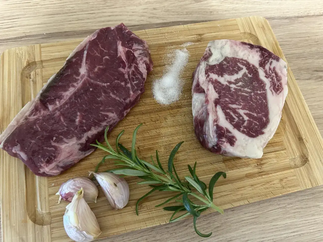 Antrykot czy rostbef? Dwa kawałki wołowiny na desce, z solą, czosnkiem i rozmarynem, czekają na idealnego steka.