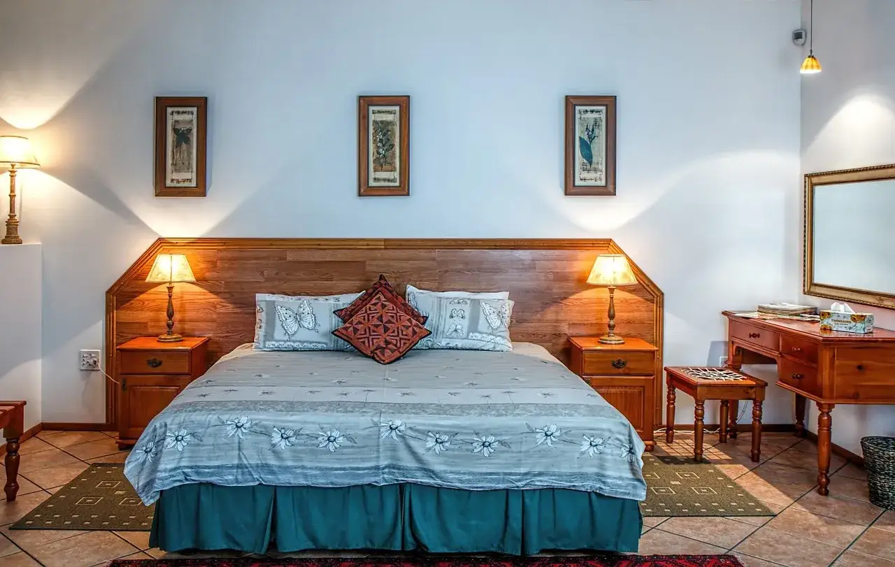 Przytulny pok&oacute;j hotelowy z dużym ł&oacute;żkiem, drewnianymi meblami i ozdobnymi obrazkami na ścianie.