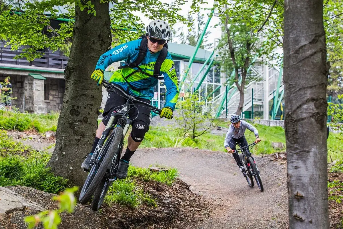 Dwóch rowerzystów zjeżdża po leśnych trasach rowerowych w Bielsku. Jeden z nich, w jaskrawej kurtce, pokonuje zakręt.
