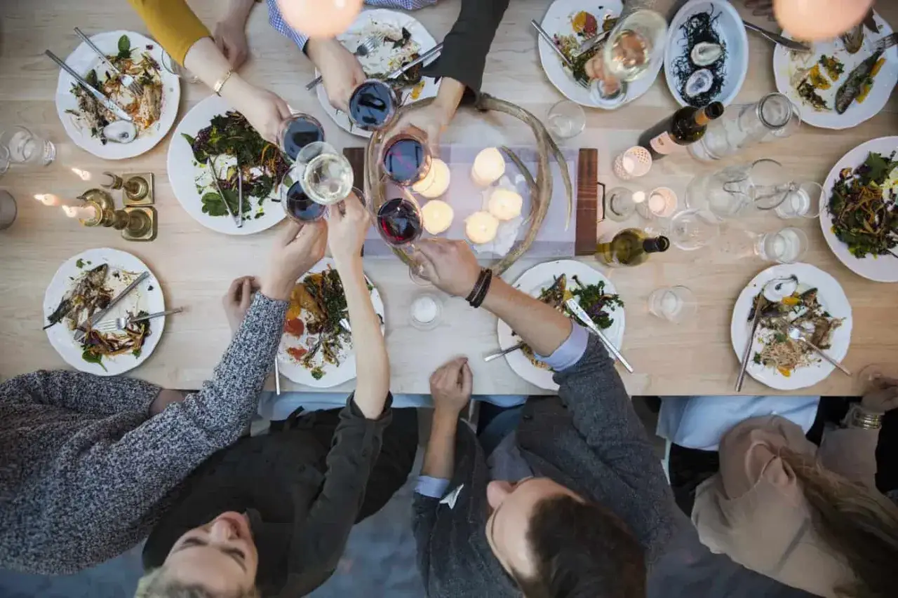 Wznoszone kieliszki i resztki jedzenia na talerzach świadczą o udanej, efektownej kolacji dla znajomych.