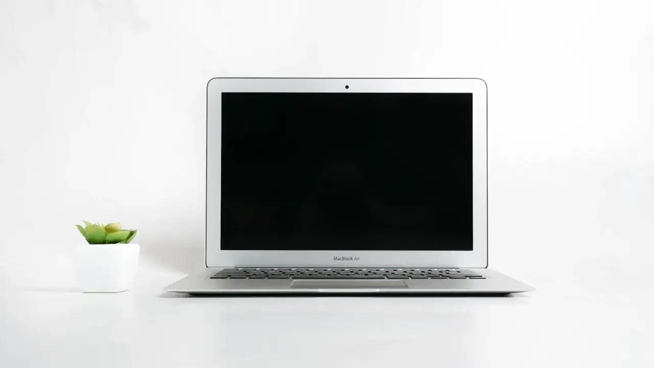 MacBook Air z wygaszonym ekranem, obok mała roślinka w białej doniczce. Dowiedz się, jak wygasić ekran w laptopie.