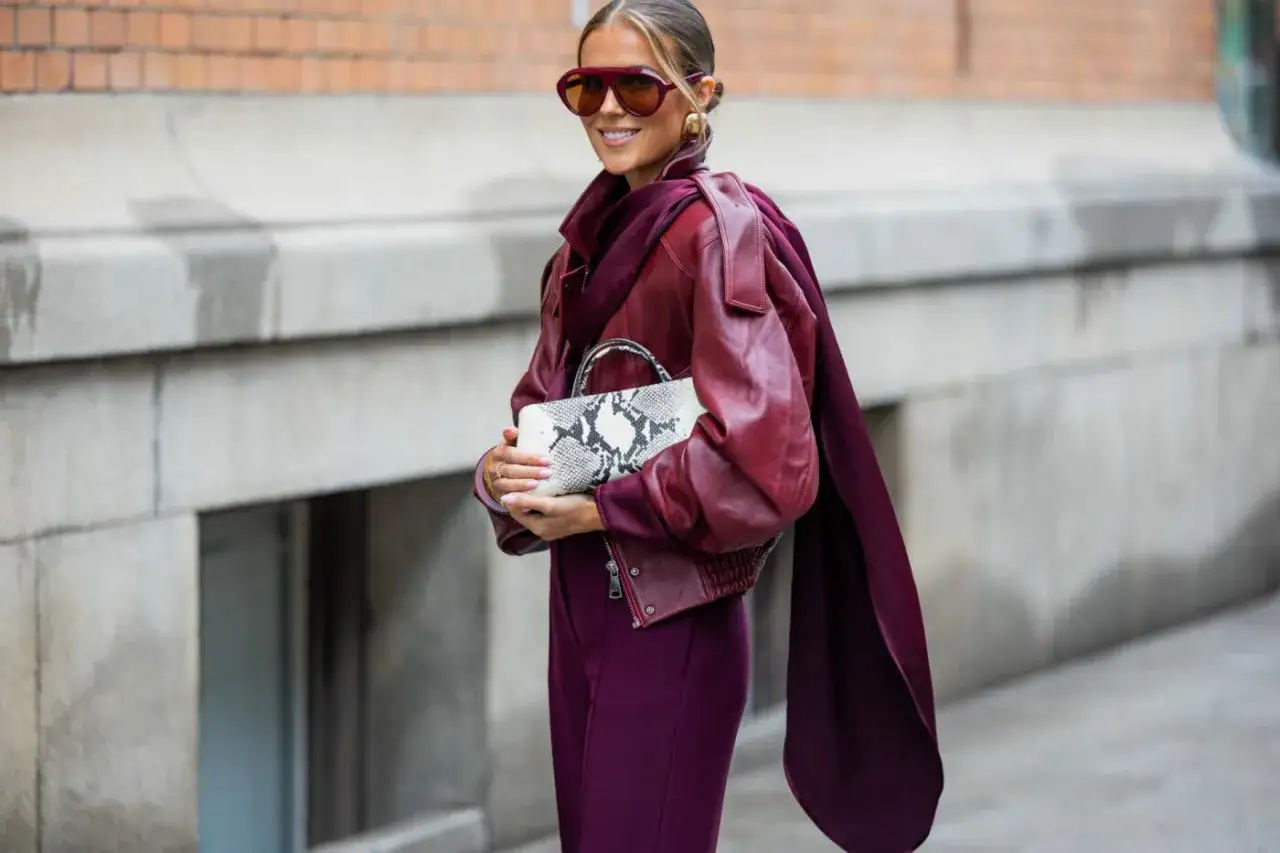 Kobieta w sk&oacute;rzanej kurtce w kolorze burgundowym i dopasowanych spodniach. Elegancka stylizacja dla pewnej siebie kobiety.