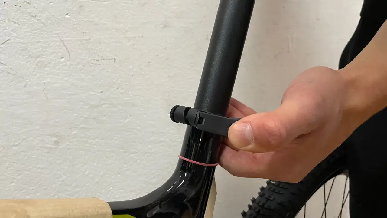 Dłoń dokręca zacisk sztycy, kończąc składanie roweru. Różowa gumka zabezpiecza ramę.