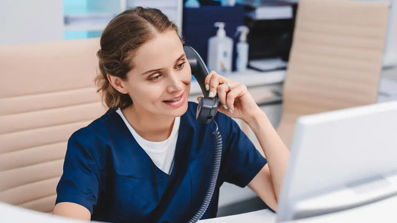 Rejestratorka medyczna z uśmiechem rozmawiająca z pacjentem, gestykulująca