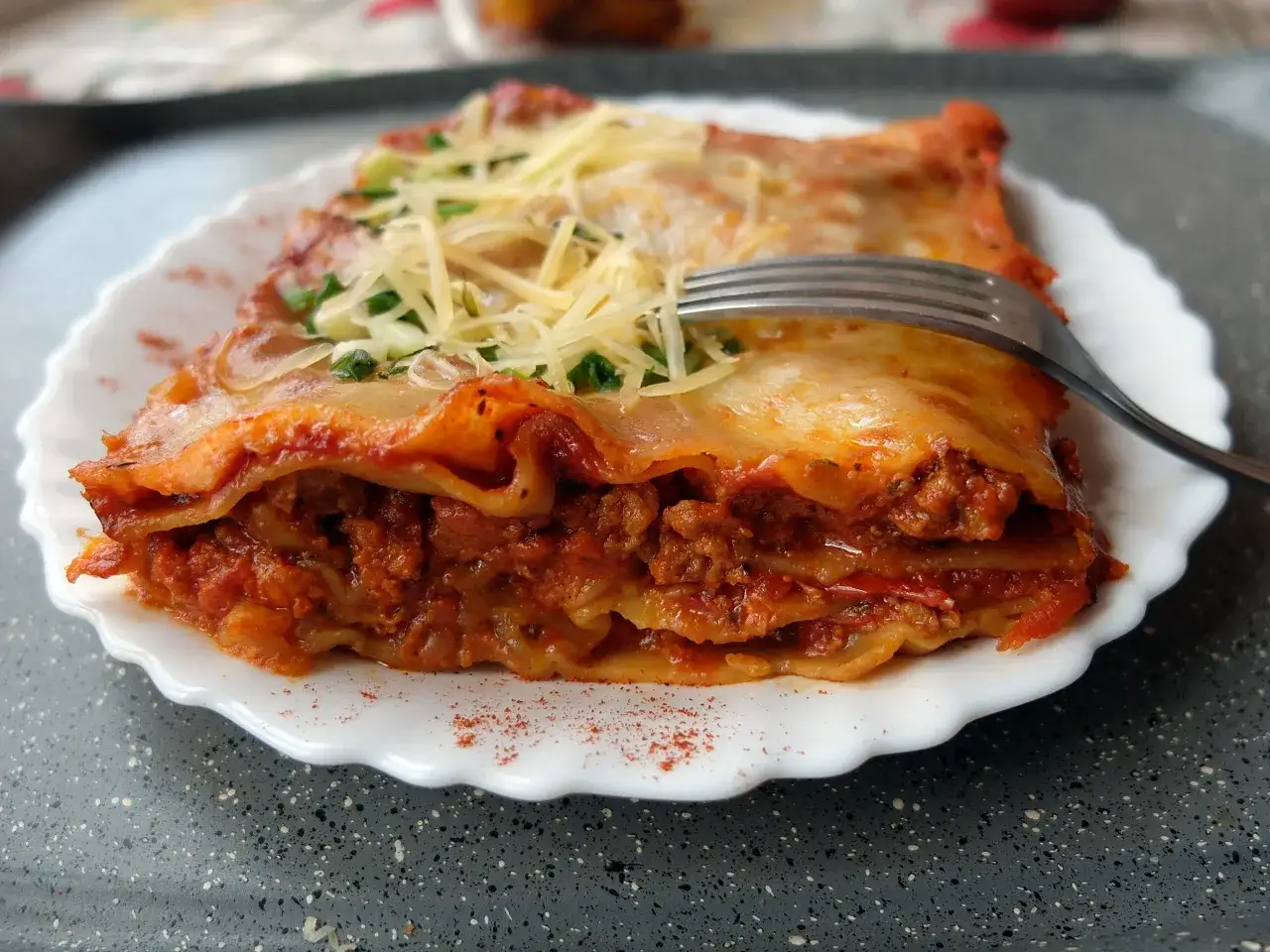 Kawałek lasagne z mięsem mielonym i sosem bolognese, posypana serem i natką pietruszki. Idealna na obiad, gdy chcesz wiedzieć, jak zrobić lasagne z mięsem mielonym i sosem bolognese.