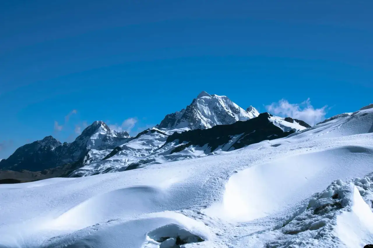 Zimowy krajobraz Nowej Zelandii: ośnieżone szczyty g&oacute;rskie pod błękitnym niebem, pokryte śniegiem stoki tworzą faliste wzory.