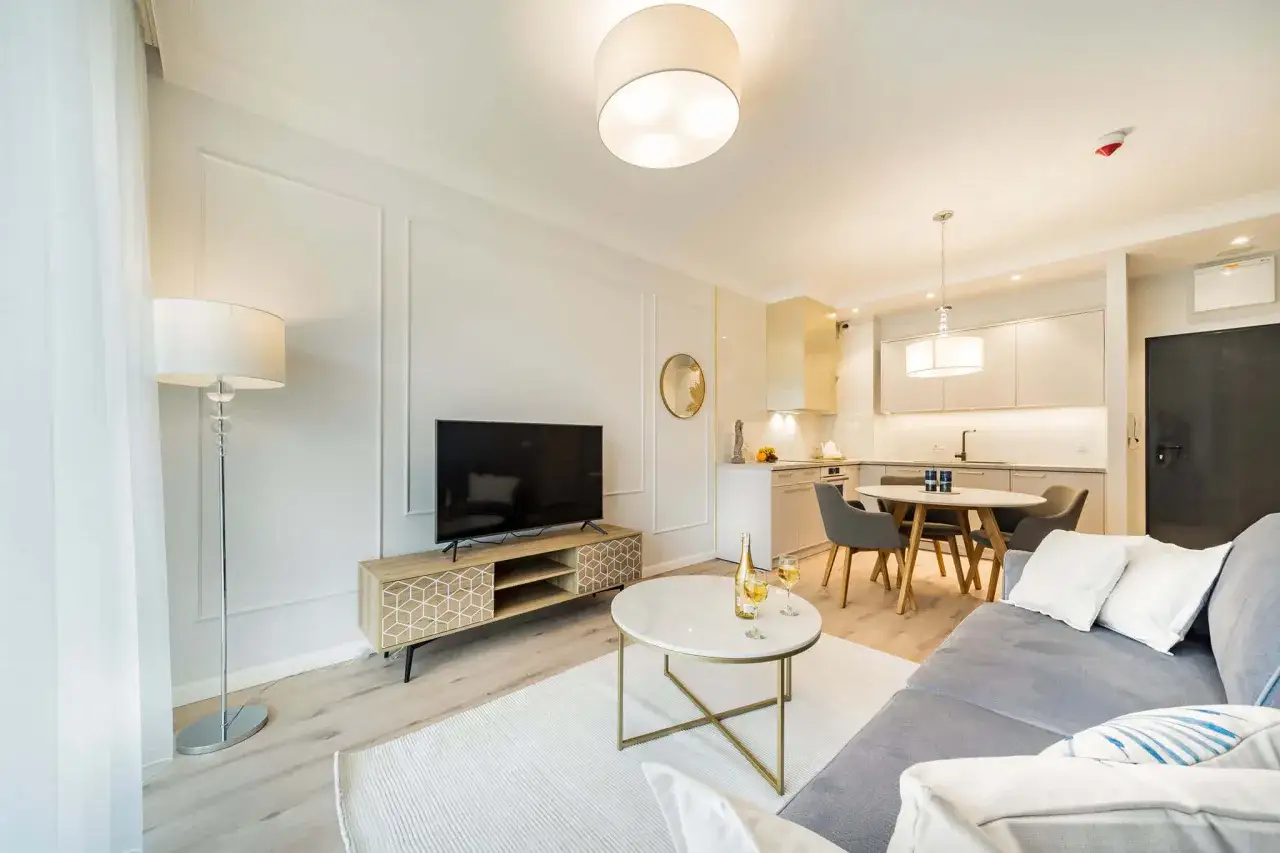 Elegancka sztukateria jak rozplanowac? Wnętrze z sofą, stolikiem kawowym, TV i aneksem kuchennym.