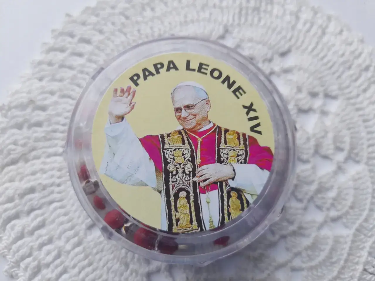 Pamiątka z Watykanu: okrągłe pudełko z wizerunkiem papieża i czerwonymi paciorkami. Idealne, by pomyśleć, co kupić w Watykanie.