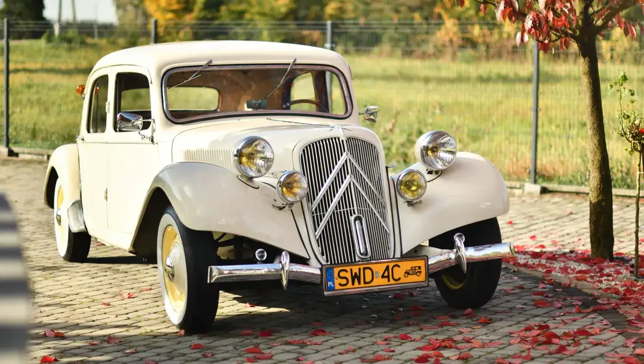 Kremowy Citroen Traction Avant, symbol przełomu w motoryzacji, na tle jesiennych liści.