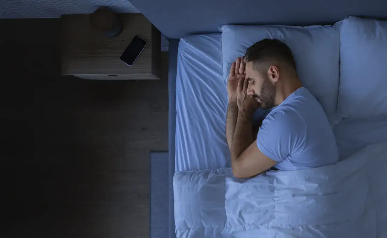 Mężczyzna śpi z rękami złożonymi na piersi, co może symbolizować nie radzenie sobie ze stresem i trudności z zasypianiem.