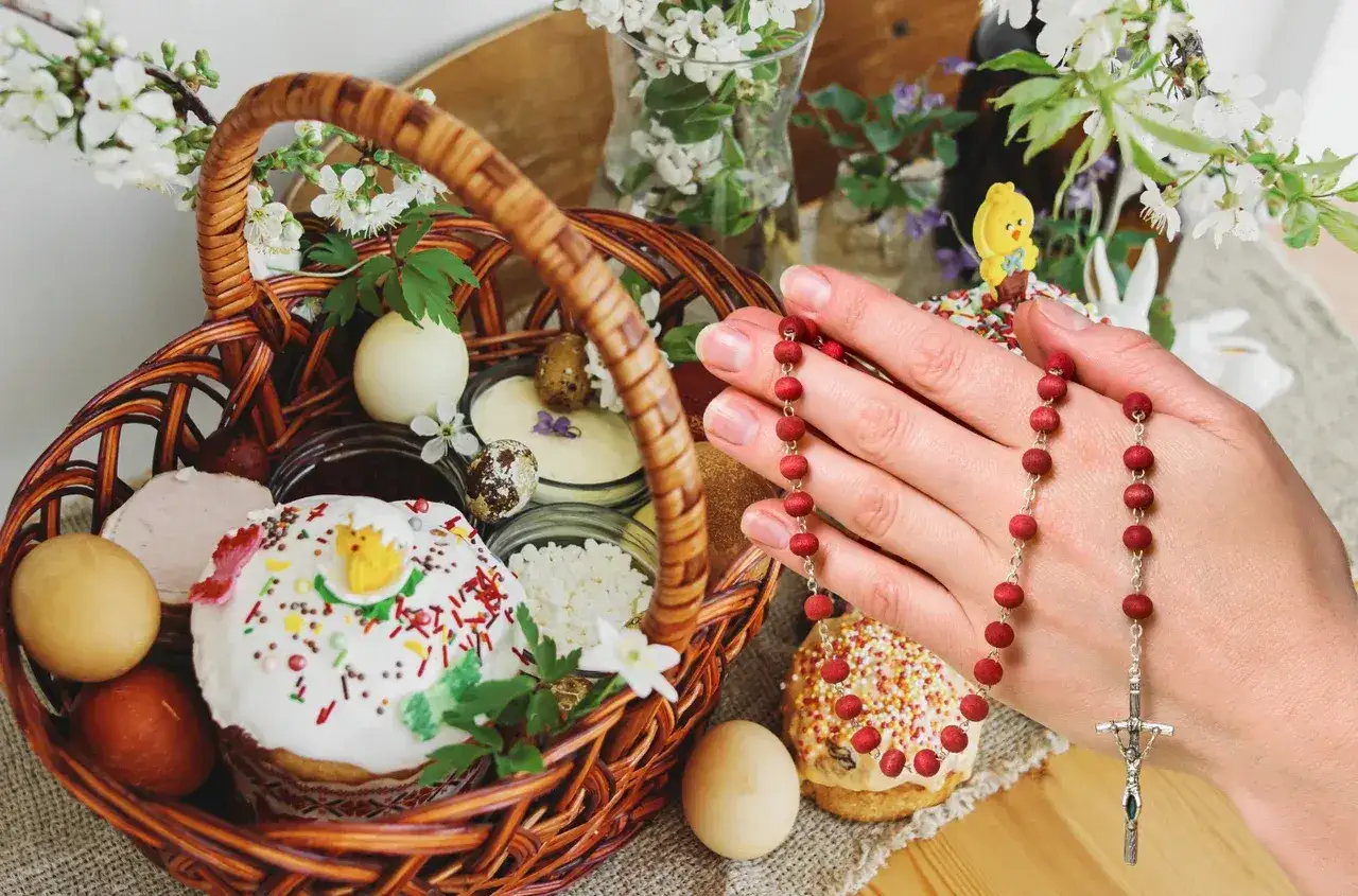 Koszyk z wielkanocnymi przysmakami i ręka trzymająca r&oacute;żaniec. Zastanawiasz się, dlaczego Wielkanoc jest ruchoma? To zależy od faz księżyca i wiosennego zr&oacute;wnania dnia z nocą.